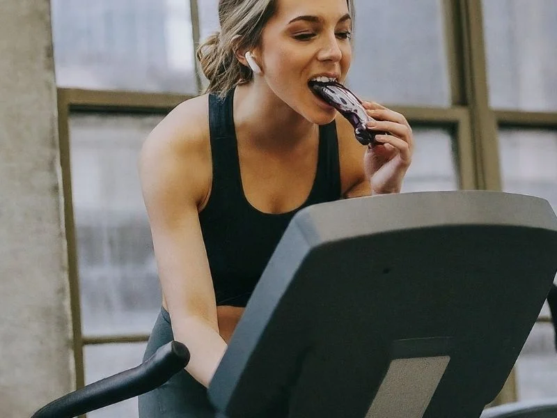 A person doing cardio while eating a protein bar