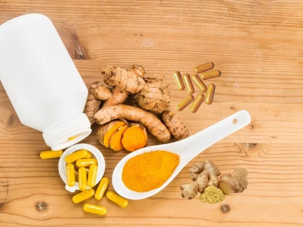 A close-up photo of a turmeric root, a piece of ginger, and a willow bark capsule]