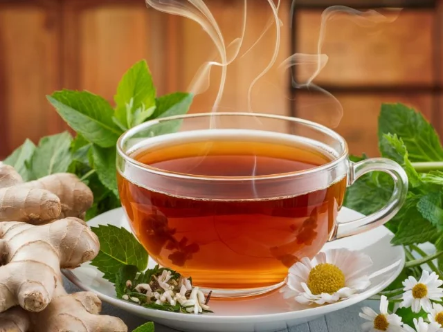 cup of herbal tea with fresh herbs like ginger, peppermint, and chamomile arranged around it