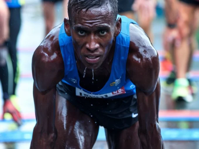 A medium shot of a marathon runner with sweat dripping from his face, pushing through a long race