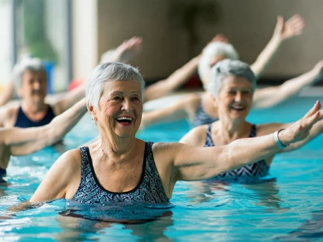 A group of seniors enjoying a water aerobics class in a brightly lit pool, smiling and engaged in the activity