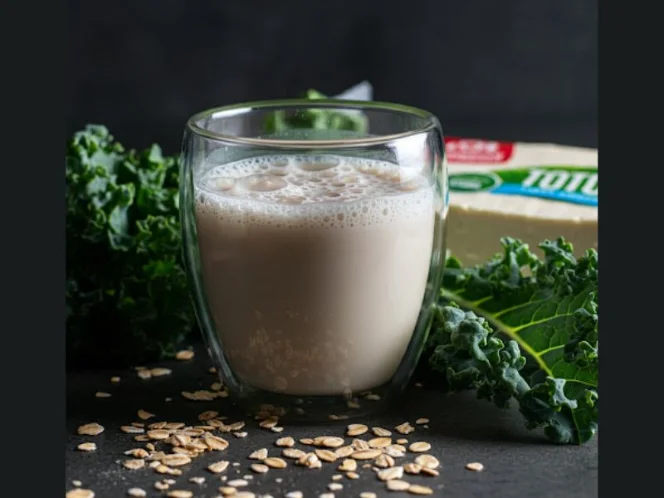 A glass of fortified plant-based milk next to a block of tofu and a bunch of leafy greens